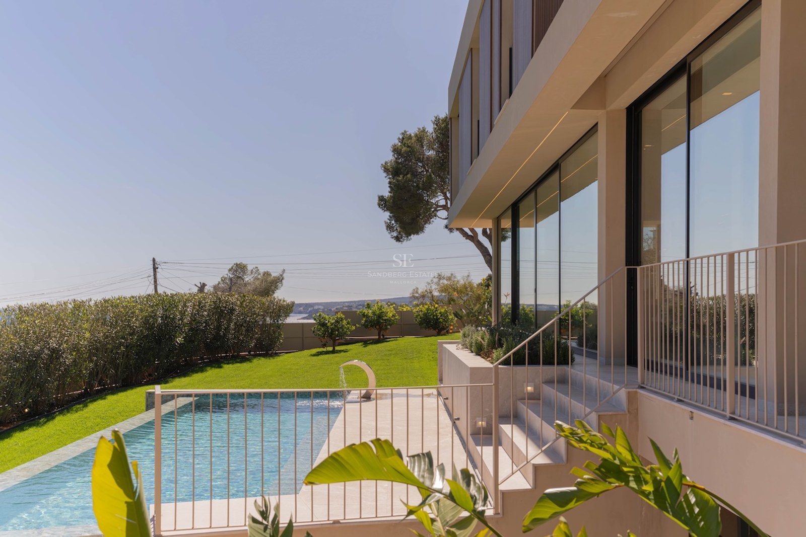 Extérieur d'une villa moderne avec piscine, pelouse et façade vitrée sous un ciel bleu clair.