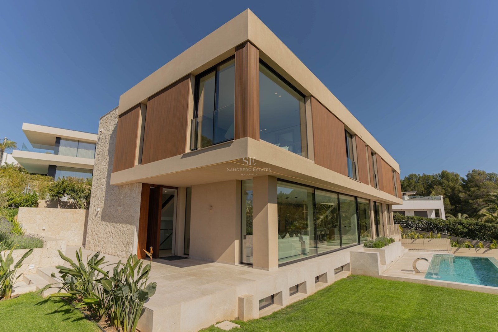 Vue extérieure d'une villa contemporaine de deux étages avec murs en pierre, baies vitrées et piscine.