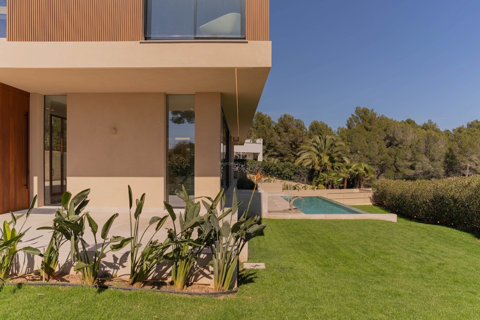 Profil latéral d'une villa moderne à deux étages avec murs couleur sable, accents en bois, pelouse et piscine.