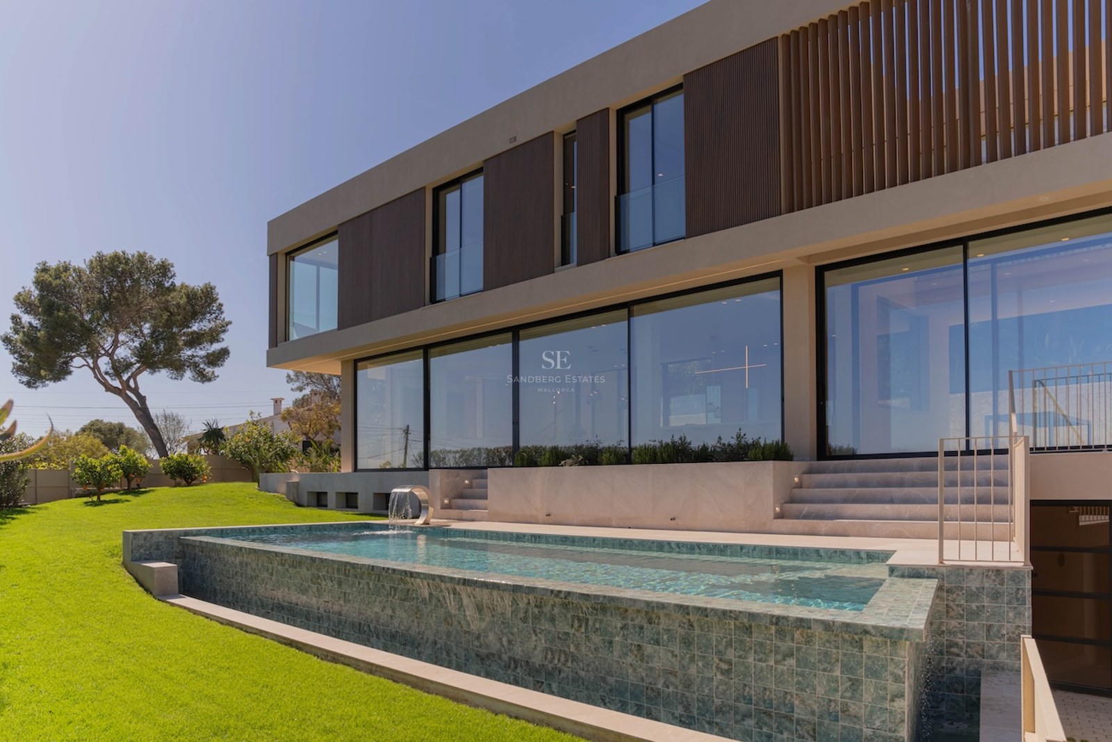Façade de villa contemporaine sur deux niveaux avec baies vitrées donnant sur une piscine en mosaïque et un jardin.