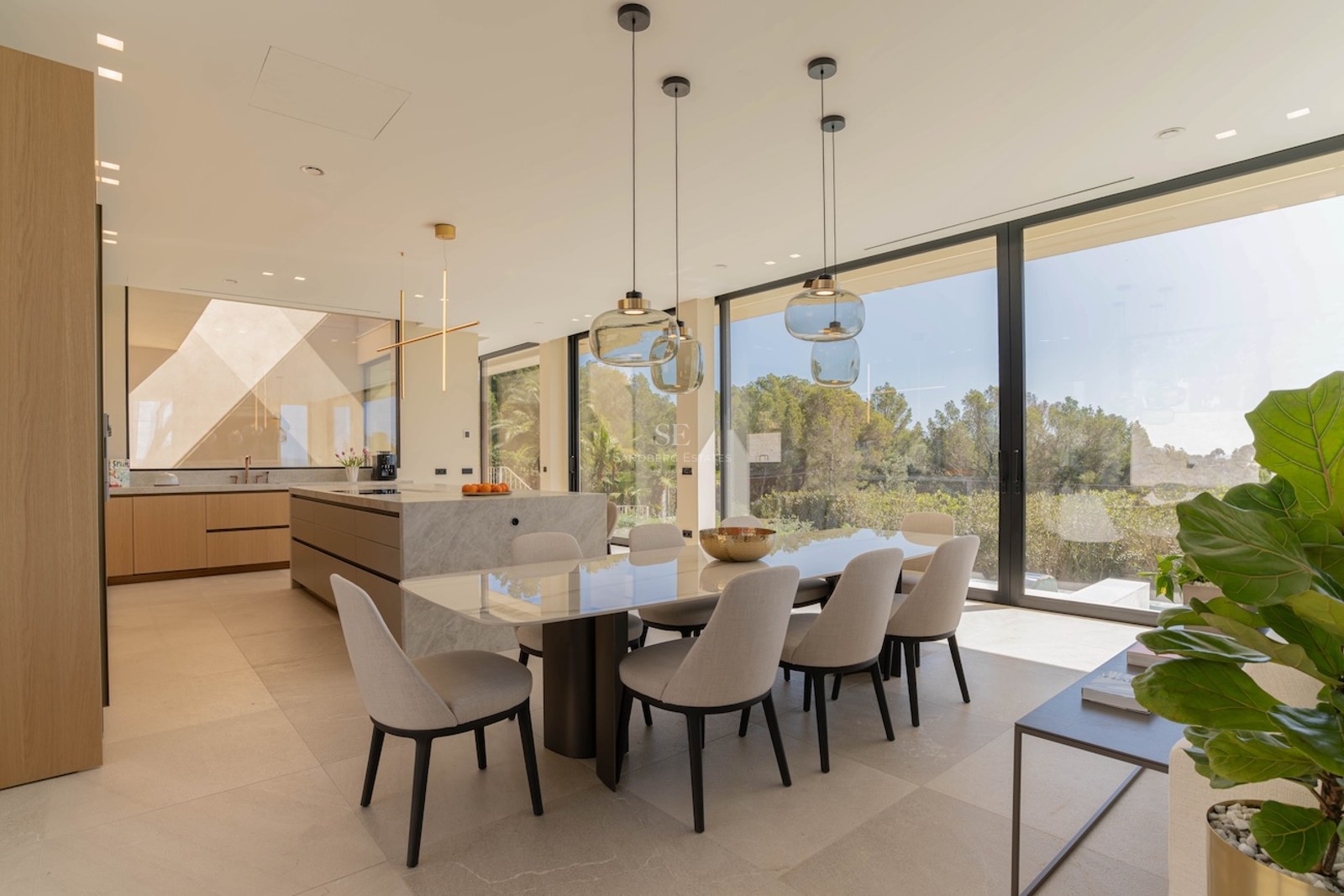 Salle à manger lumineuse avec table en marbre et baies vitrées donnant sur un paysage verdoyant.