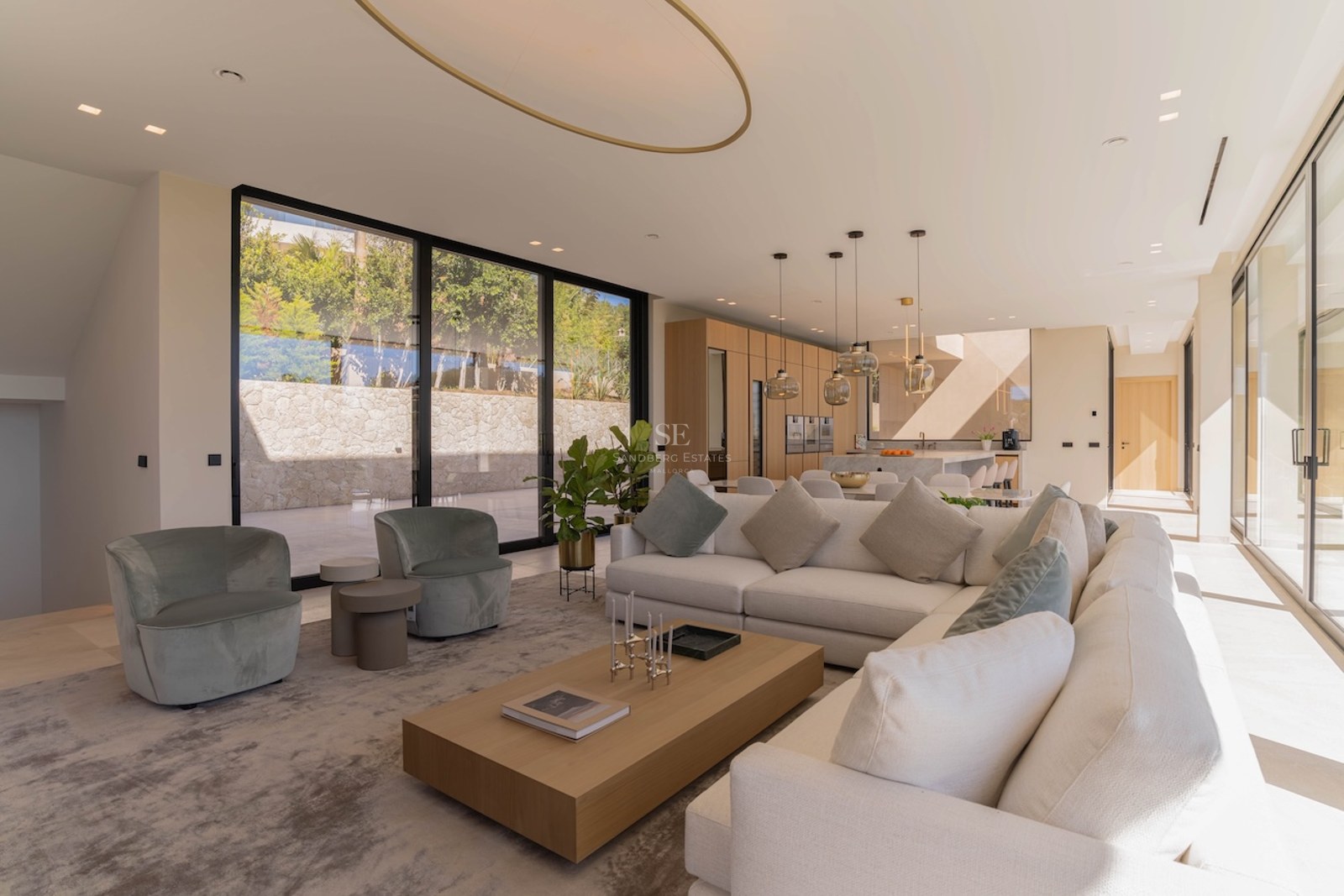Salon moderne spacieux avec canapé en L crème, table basse en bois et grandes baies vitrées.