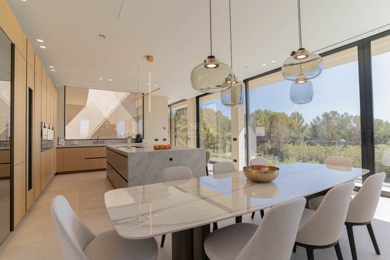 Cuisine moderne avec îlot en marbre et table à manger près de grandes baies vitrées donnant sur la nature.