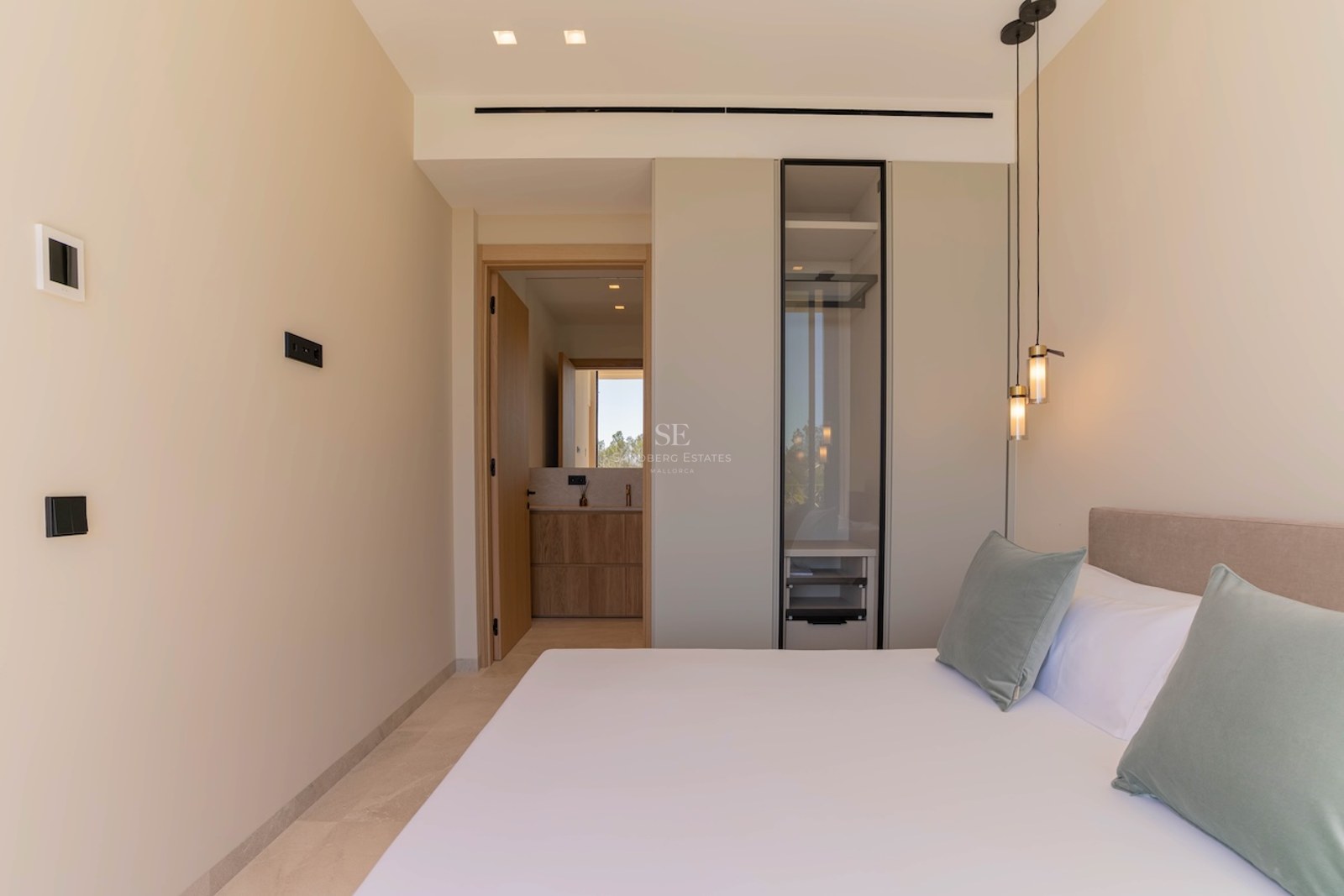 Chambre moderne aux tons neutres avec armoire vitrée intégrée et aperçu de la salle de bain privée.
