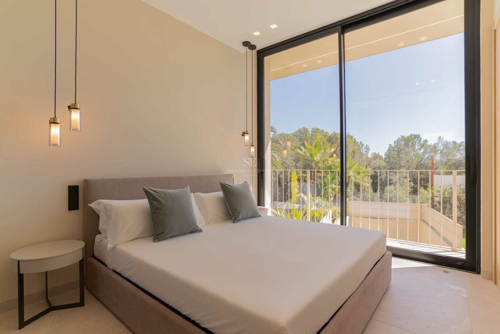 Chambre contemporaine avec de grandes baies vitrées, un lit aux tons neutres et une vue sur les arbres.