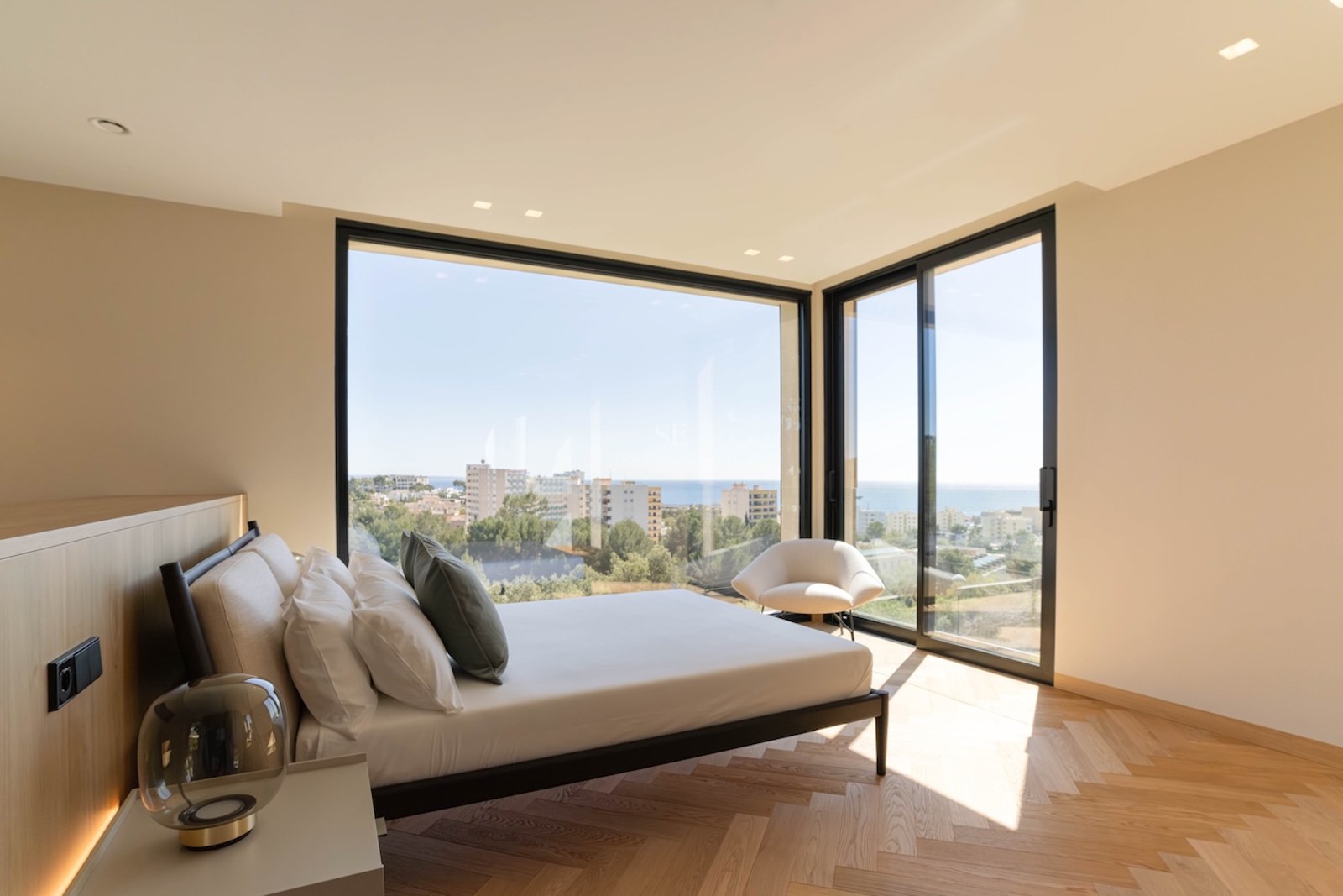 Chambre principale lumineuse avec fenêtres d'angle du sol au plafond, vue sur la mer et parquet en chevrons.
