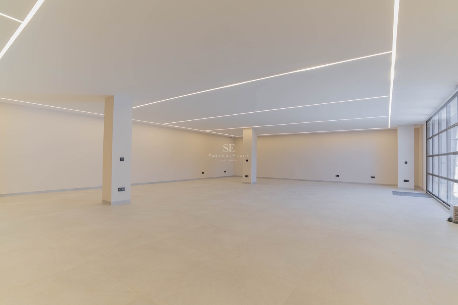 Grand sous-sol moderne et vide avec murs blancs, sol en béton poli et éclairage LED linéaire au plafond.