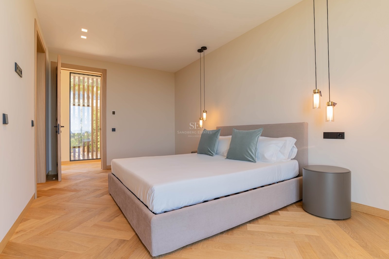 Chambre moderne avec lit rembourré, parquet en chêne en chevrons, luminaires suspendus et tons neutres.