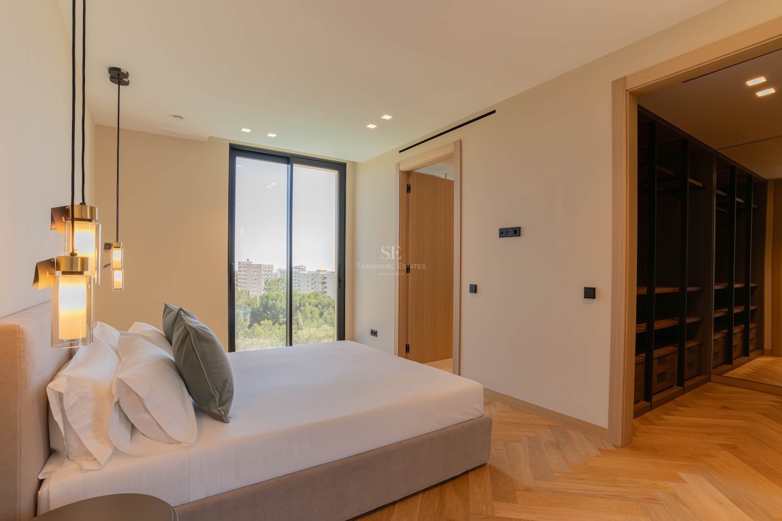 Chambre principale moderne avec parquet en chêne en chevrons, baies vitrées et un grand dressing intégré en bois sombre.