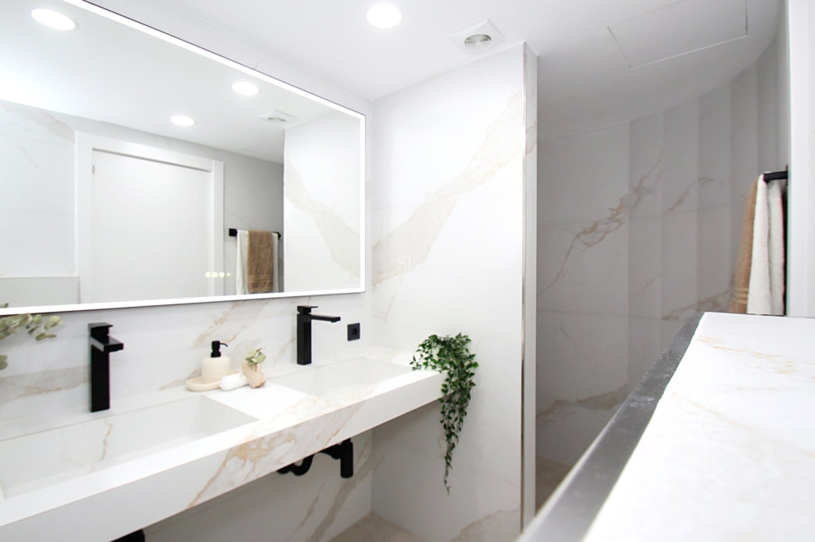 Baño luminoso con lavabo doble de mármol blanco, grifería negra mate y un gran espejo retroiluminado.