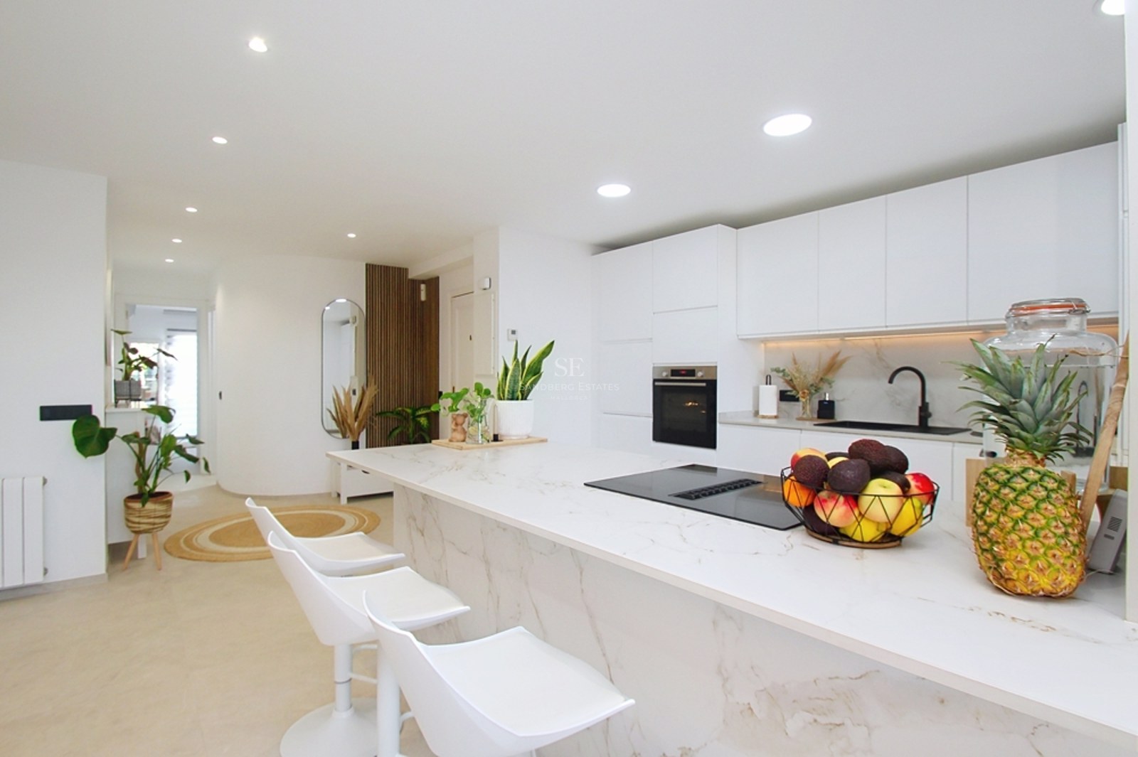 Cocina minimalista blanca con isla de efecto mármol, taburetes de diseño y electrodomésticos integrados.