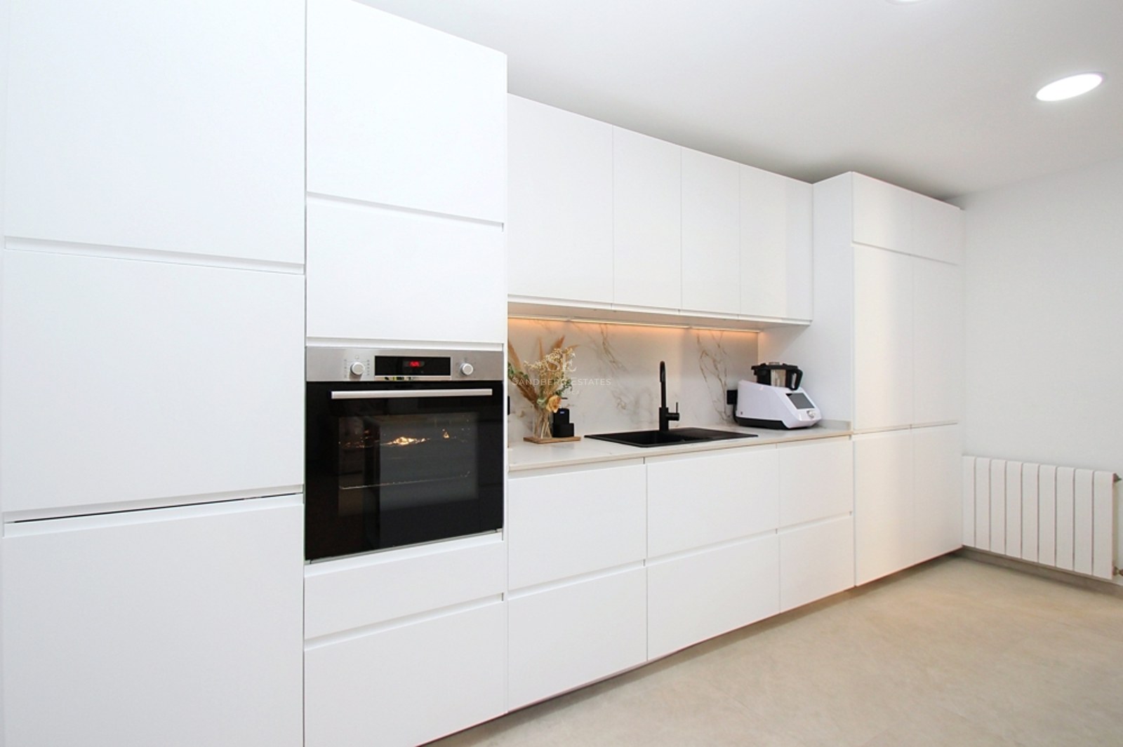 Cocina contemporánea blanca con armarios sin tiradores, grifería negra y horno de acero inoxidable integrado.