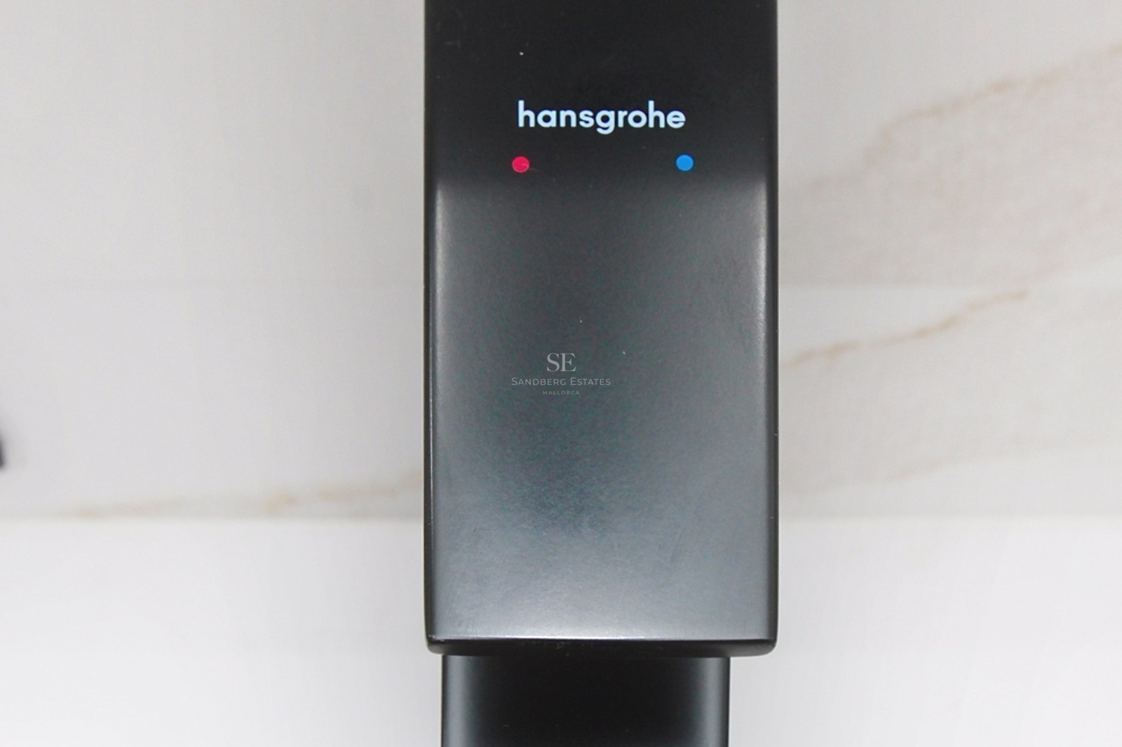 Primer plano de un grifo Hansgrohe en acabado negro mate sobre fondo de mármol blanco.