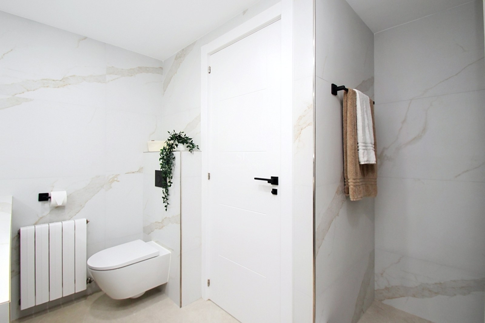 Baño moderno con azulejos de gran formato efecto mármol, inodoro suspendido y detalles en negro mate.