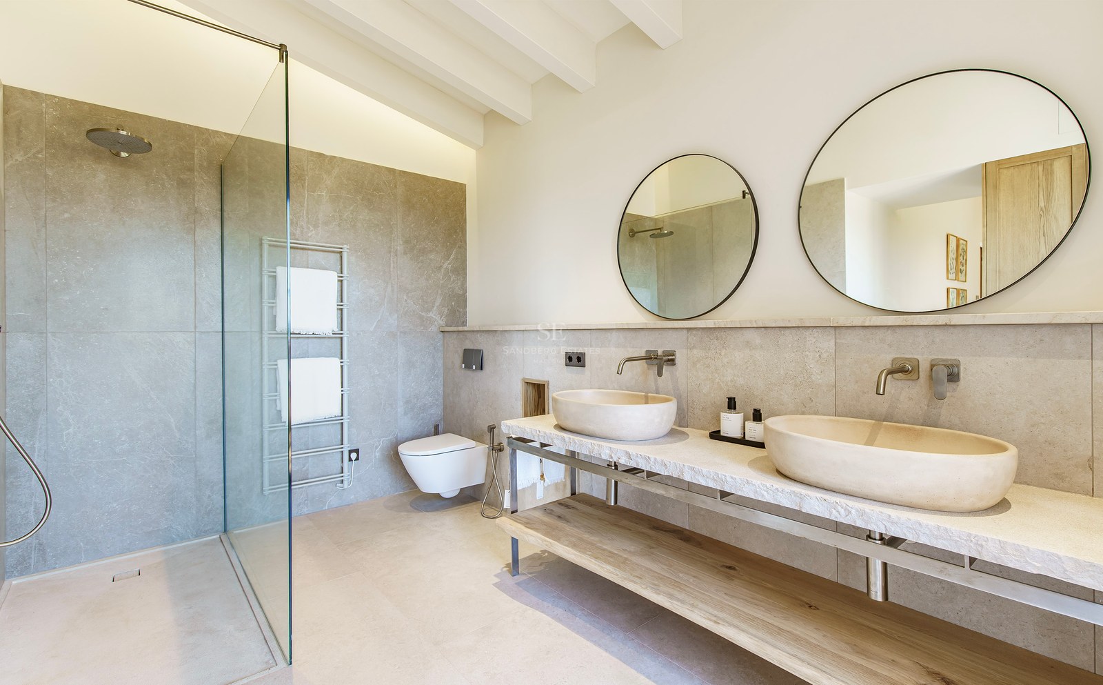 Luxuriöses Badezimmer mit zwei Steinwaschbecken auf Marmorplatte, Rundspiegeln und begehbarer Glasdusche.