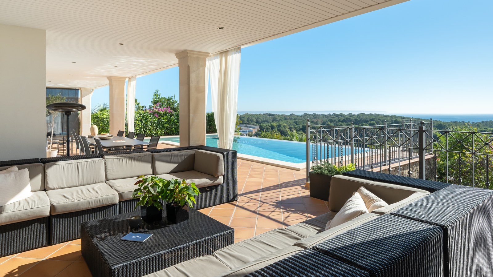 Terrasse de luxe ombragée avec canapés en osier, sol en terre cuite et piscine à débordement sur la mer.