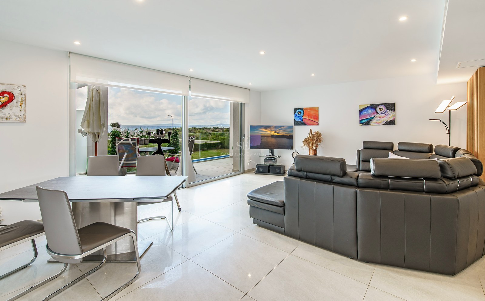 Salon moderne avec canapé en cuir gris foncé, coin repas et grandes baies vitrées ouvrant sur une vue mer.