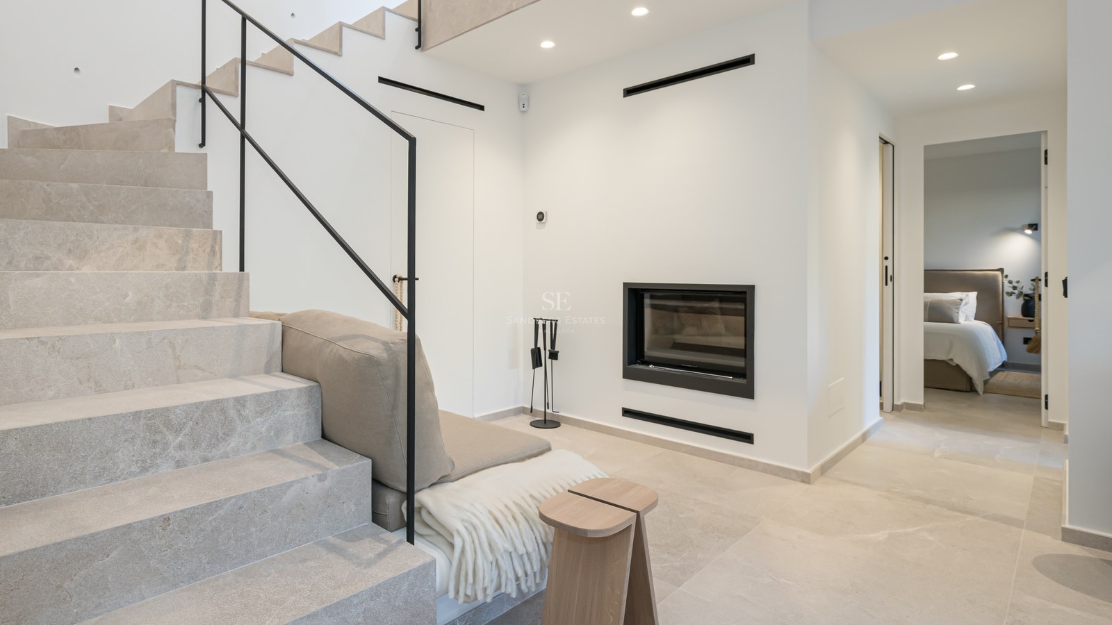 Intérieur moderne avec escalier en pierre claire, rampe noire minimaliste et cheminée murale intégrée.