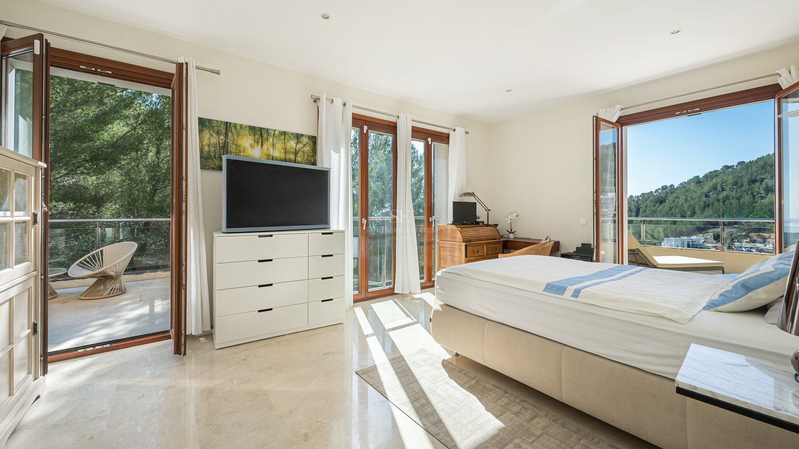 Dormitorio luminoso con suelo de mármol, cama doble y puertas de cristal a una terraza con vistas al monte.