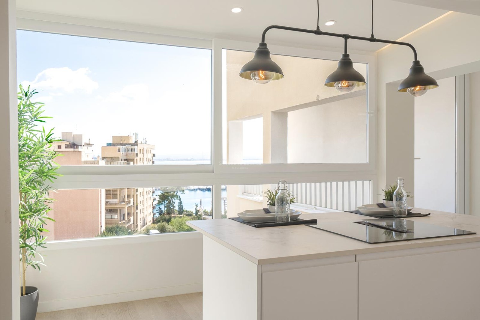 Îlot de cuisine blanc avec plaque de cuisson devant une fenêtre offrant une vue sur le port et la ville.