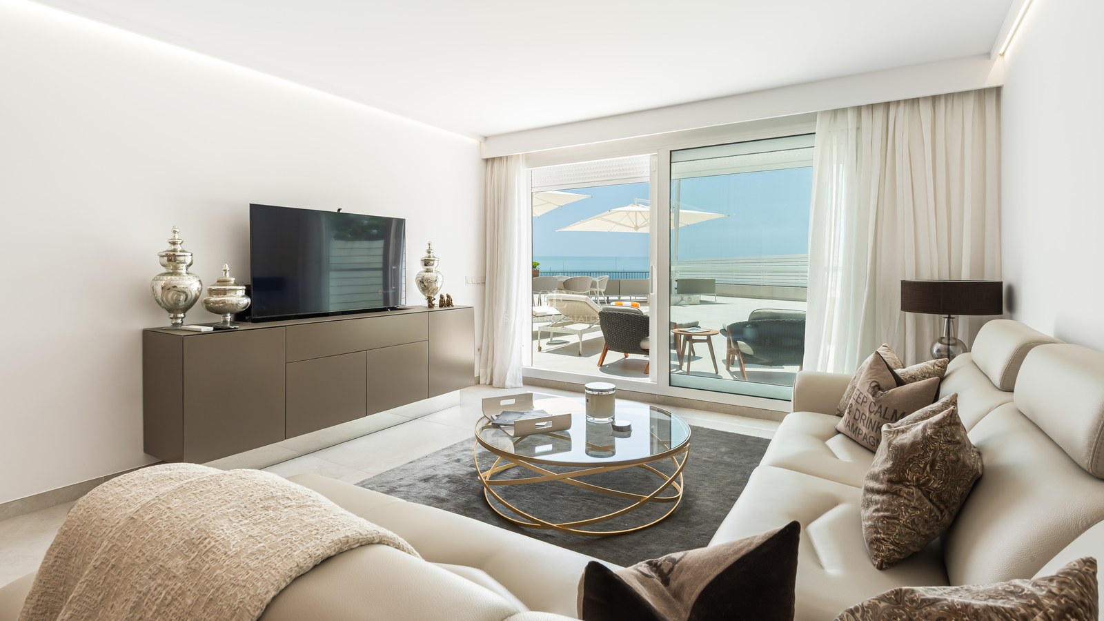 Modern living room featuring cream leather sofas, a round glass coffee table, and large sliding doors opening to a terrace.