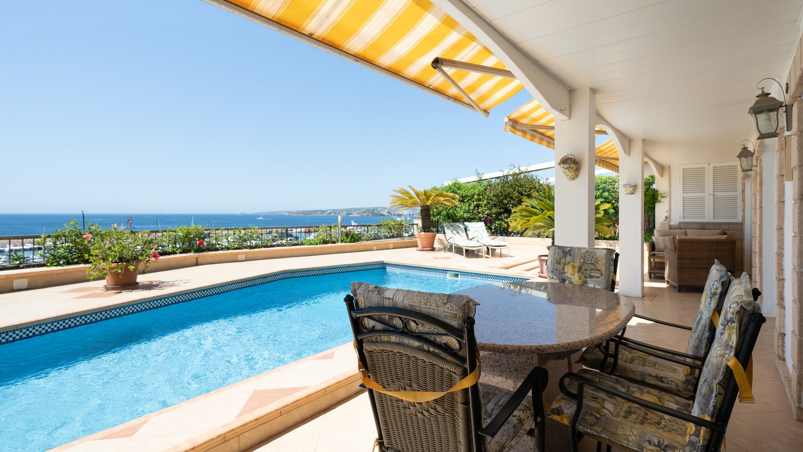 Outdoor terrace featuring a blue swimming pool, dining set, and yellow awnings with panoramic ocean views.