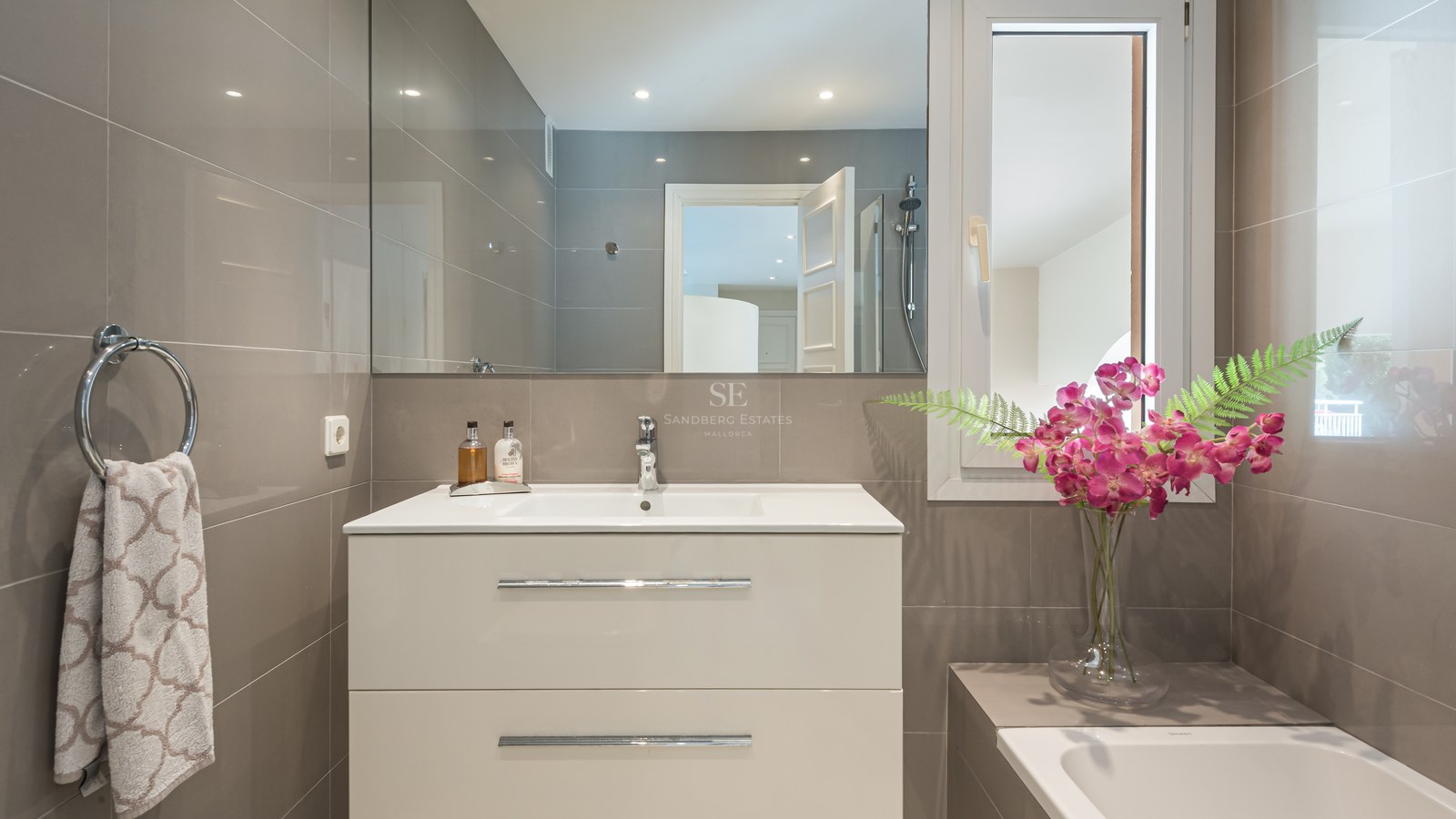 Salle de bains contemporaine avec meuble vasque blanc, grand miroir et carrelage taupe avec accents chromés.