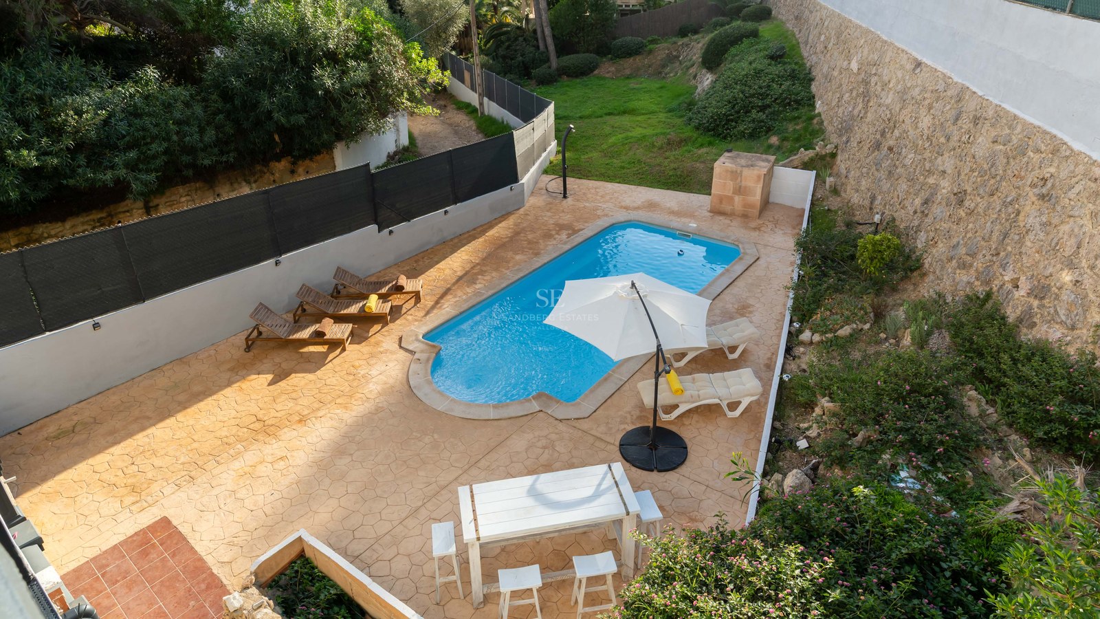 Overhead view of a turquoise swimming pool surrounded by a terracotta patio, sun loungers, and an outdoor dining area.