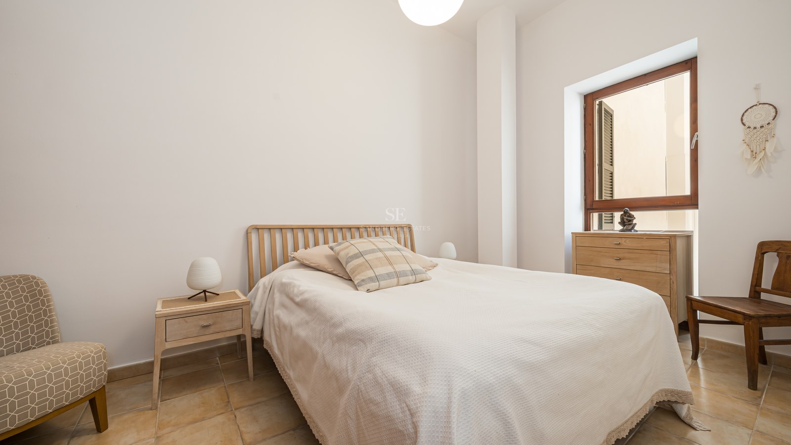 Chambre minimaliste avec sol en terre cuite, meubles en bois clair et fenêtre à cadre en bois naturel.