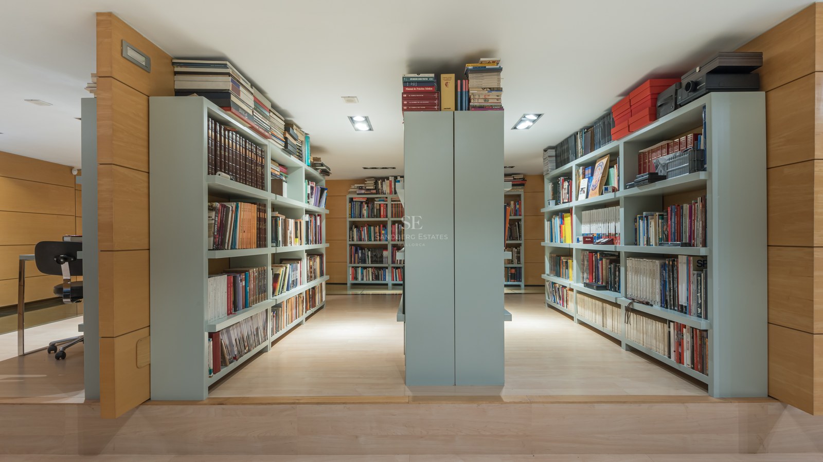 Modernt hembibliotek med ljus ekpanel och omfattande platsbyggda hyllor i salviagrönt.