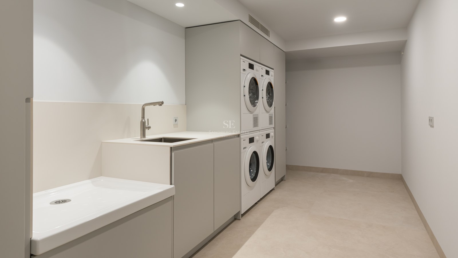 Buanderie moderne équipée de lave-linge et sèche-linge Miele, rangements épurés et grand bac de lavage.