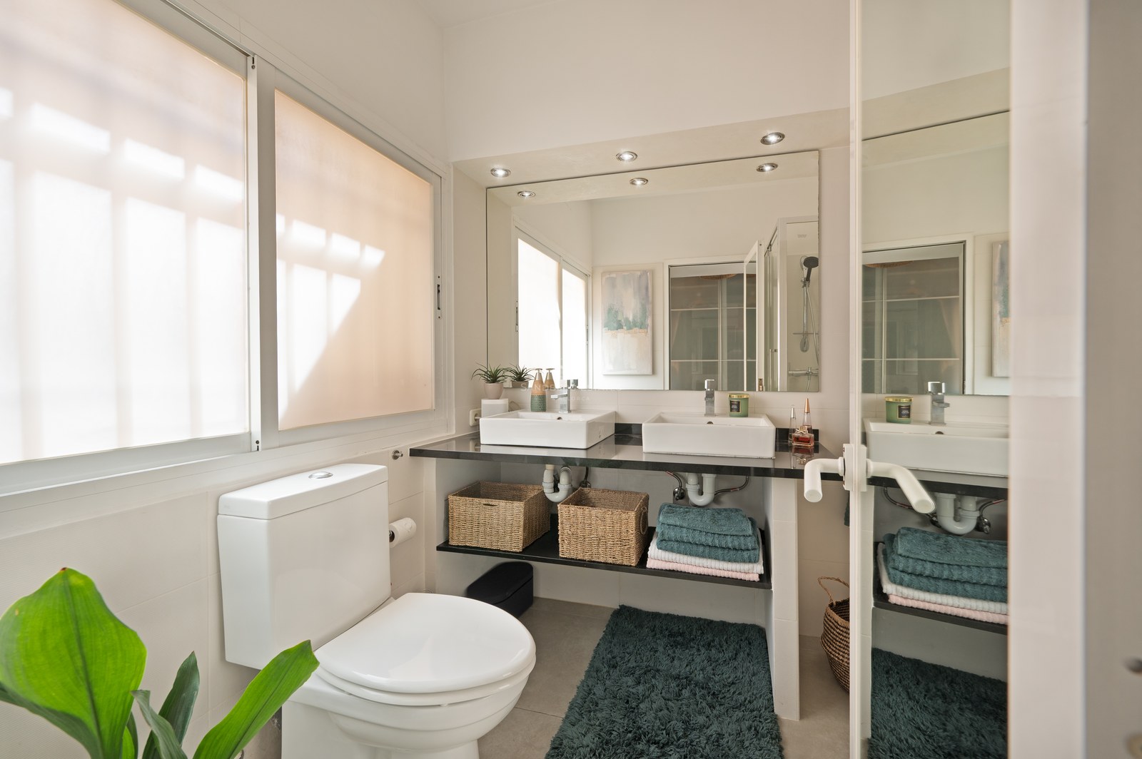 Bright bathroom with double vessel sinks, dark stone countertop, large mirror, and natural light from a window.