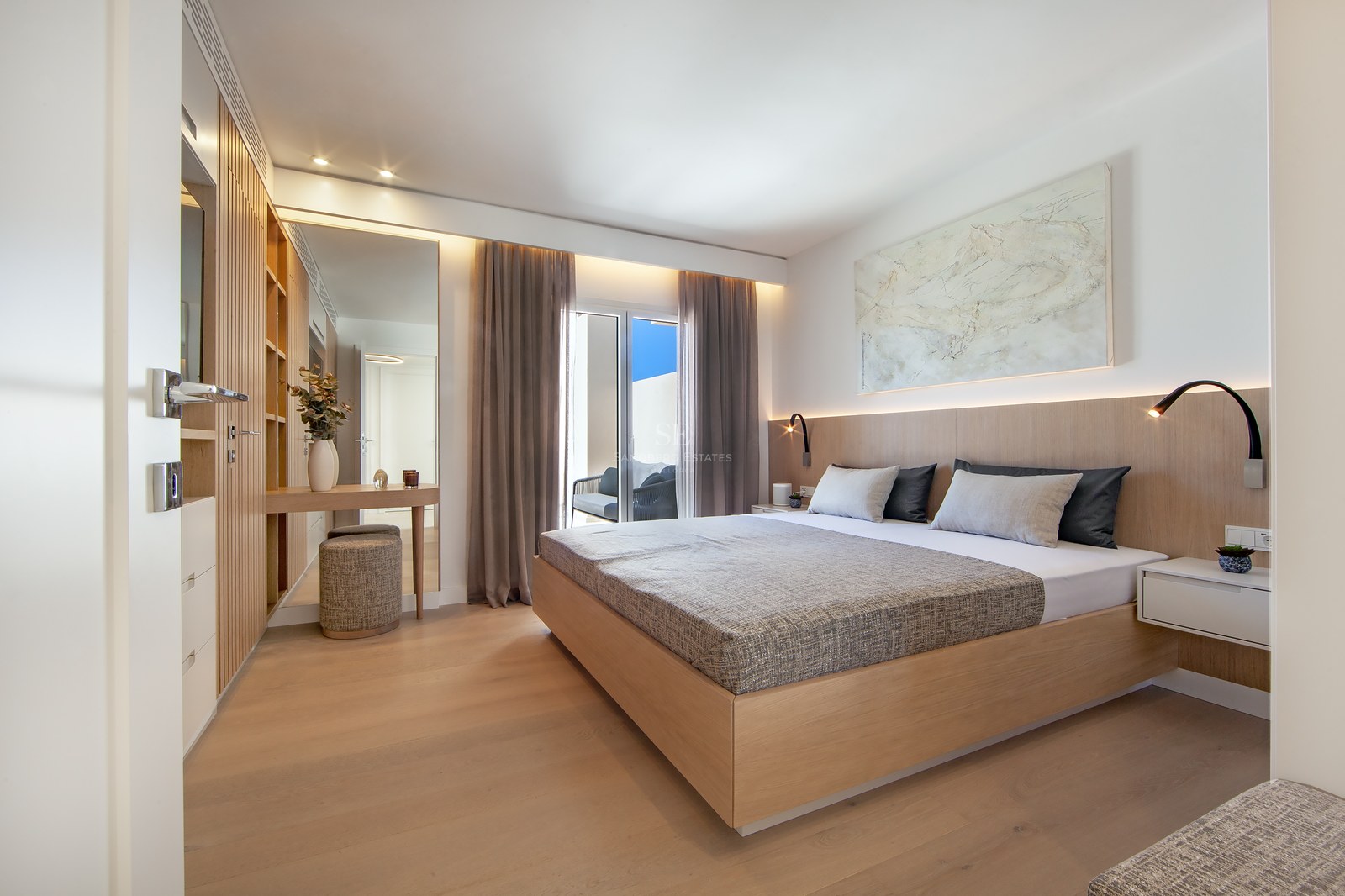 Modern master bedroom with a large wooden bed, integrated lighting, wood paneling, and access to a sunny balcony.