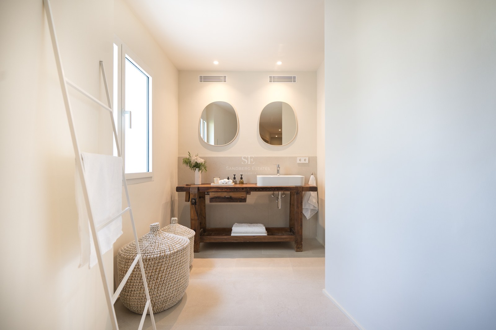 Salle de bains moderne avec meuble en bois de récupération, vasque à poser, miroirs organiques et paniers en osier.