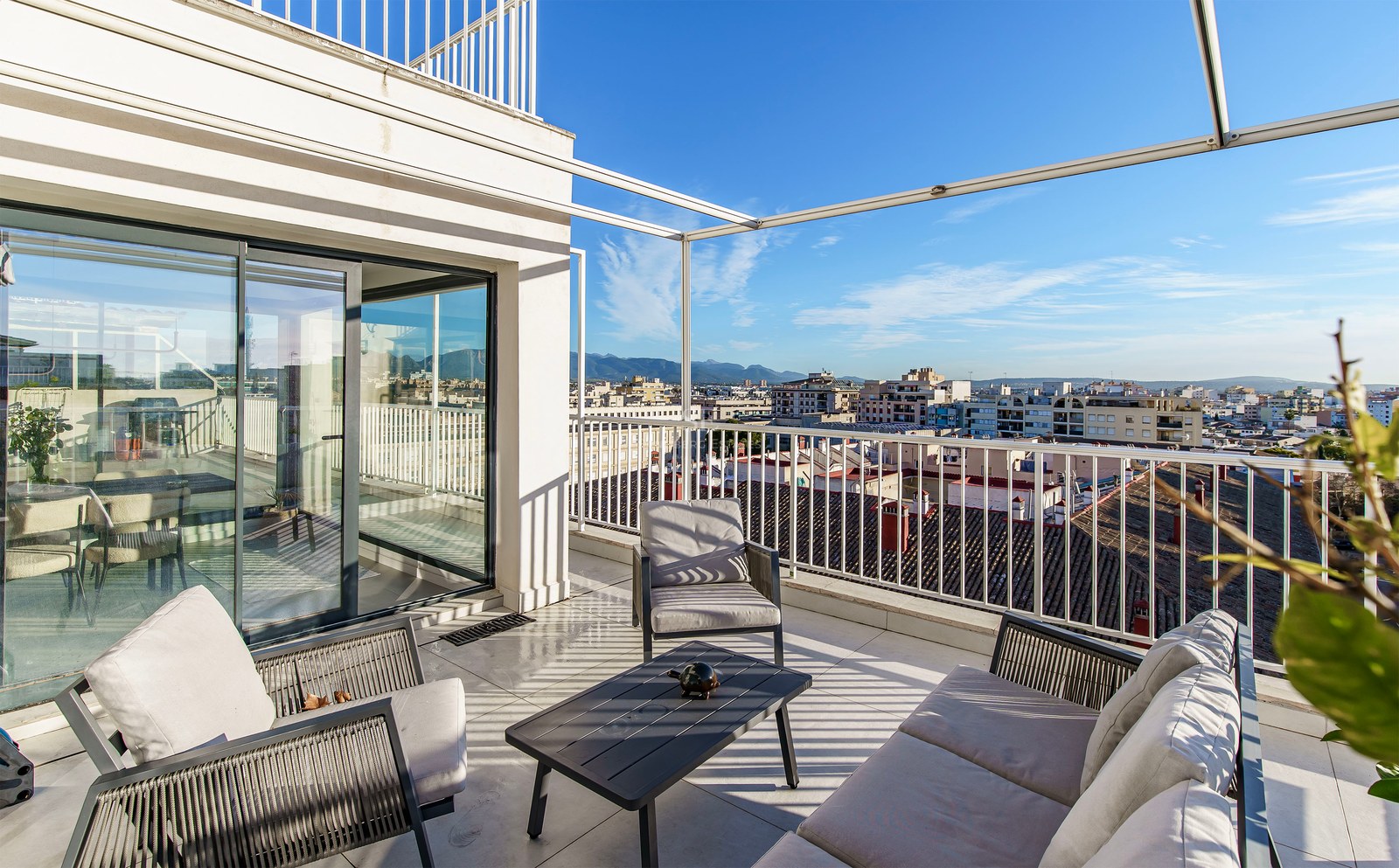 Grande terrasse blanche avec canapé et fauteuils d'extérieur modernes surplombant la ville et les montagnes.