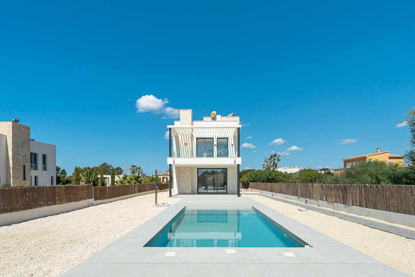 Piscine rectangulaire bleue menant à une villa moderne blanche de deux étages sous un ciel bleu pur.