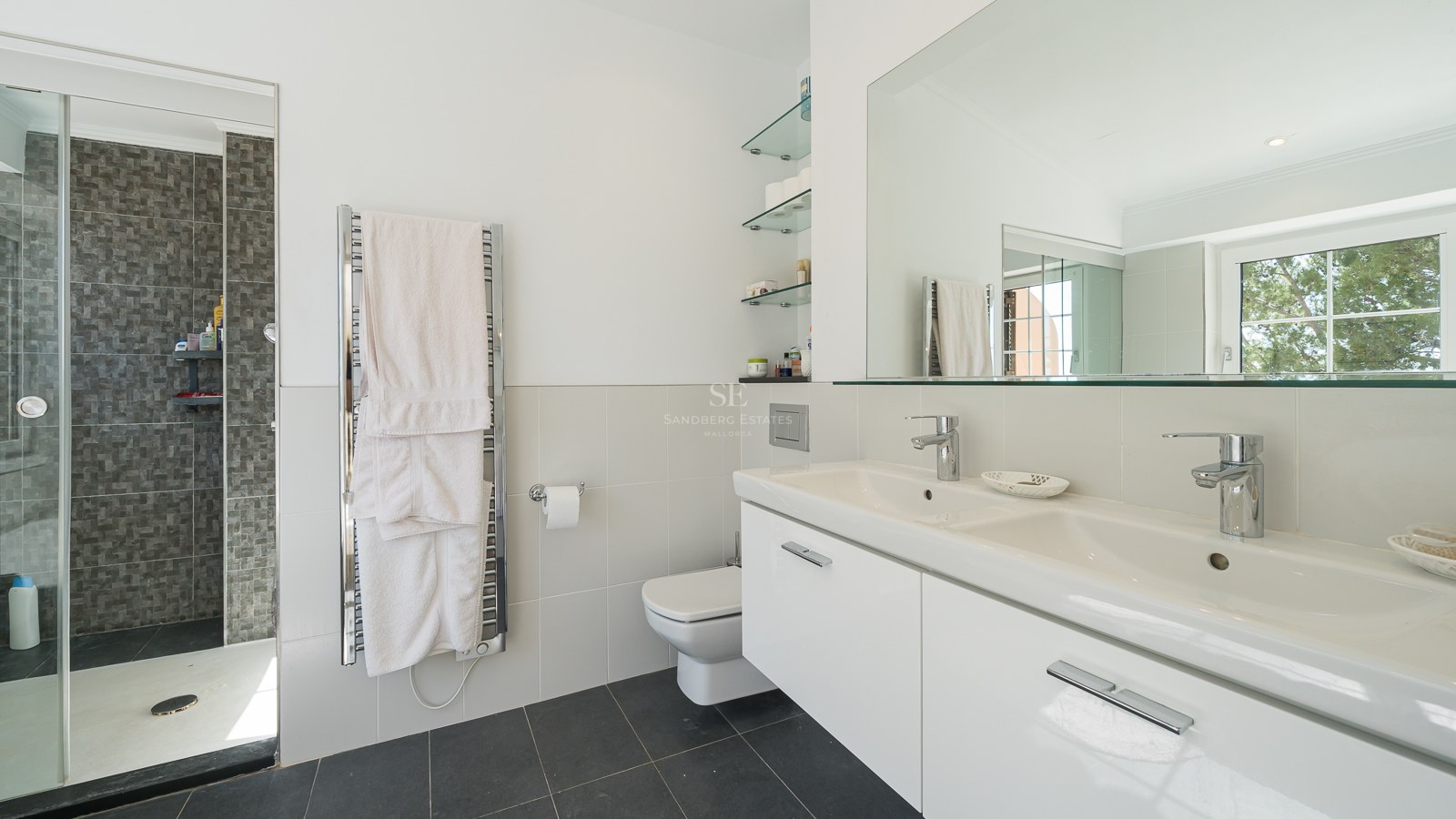 Salle de bain moderne avec double vasque blanche, grand miroir, sèche-serviettes et douche à l'italienne.