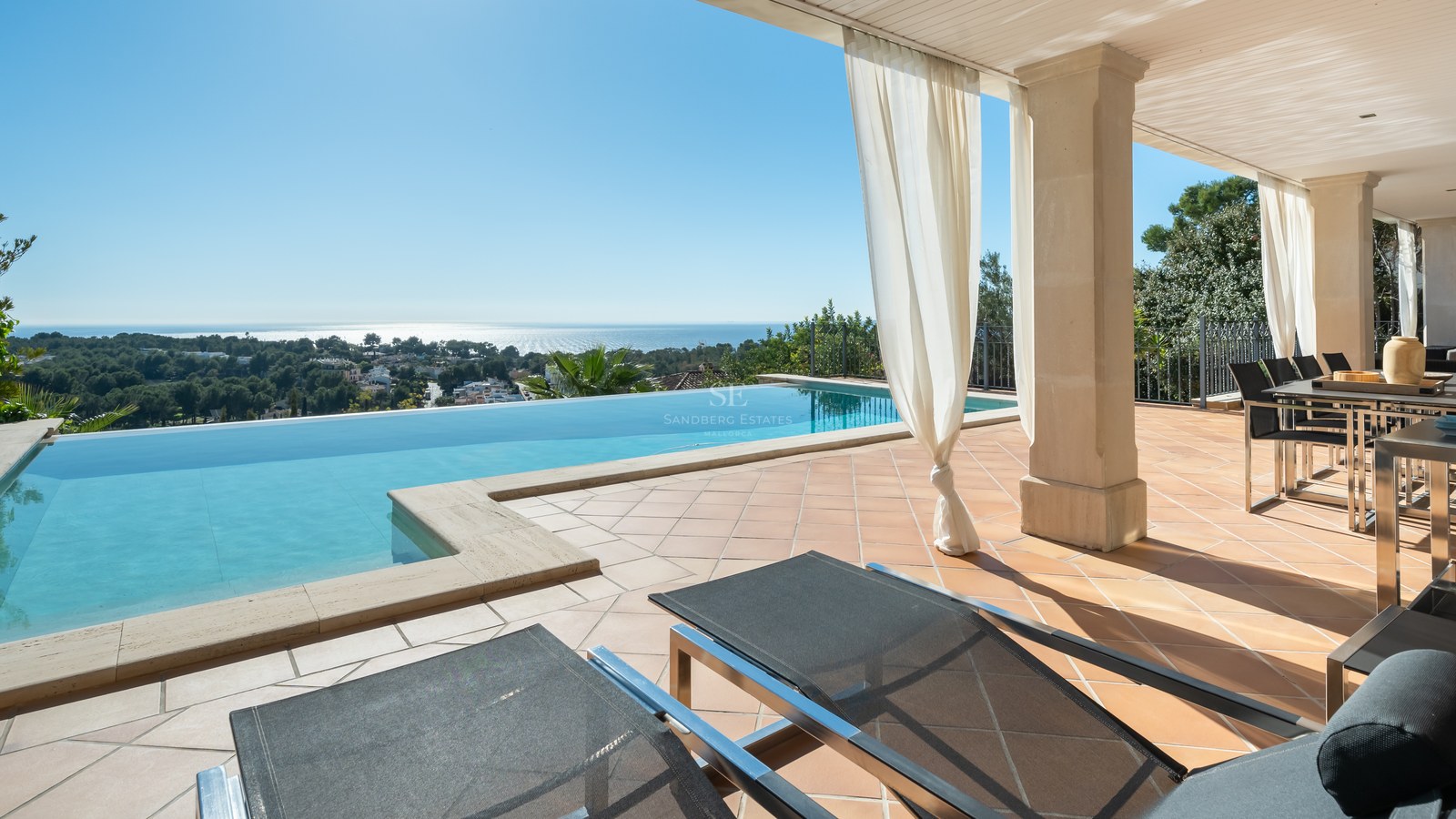 Piscine à débordement sur terrasse en terre cuite avec vue sur la Méditerranée et coin repas ombragé.