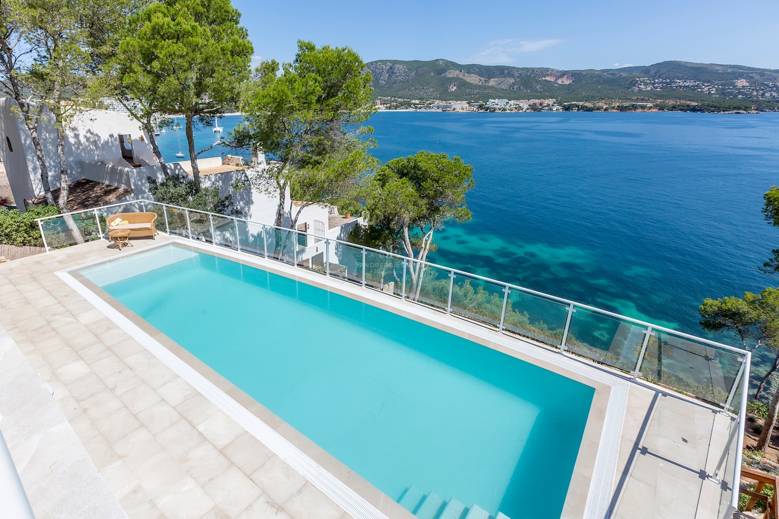 An elevated view of a turquoise infinity pool overlooking the Mediterranean sea with mountains in the background.