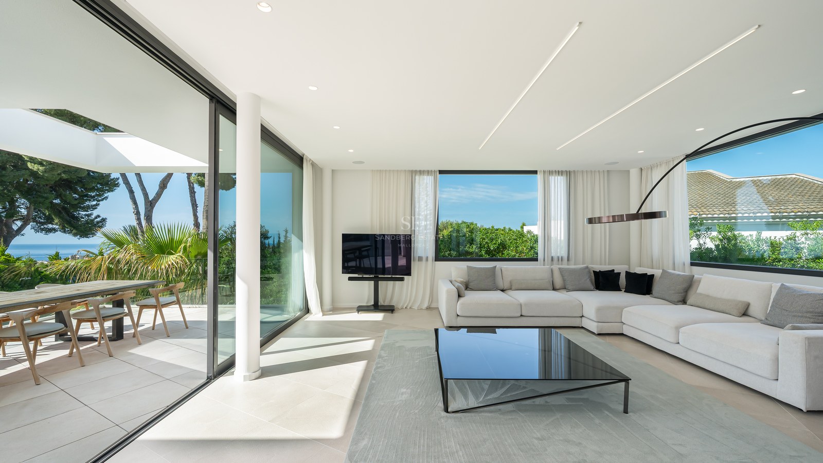 Salon moderne et lumineux avec de grandes baies vitrées ouvrant sur une terrasse avec vue mer et un canapé d'angle blanc.