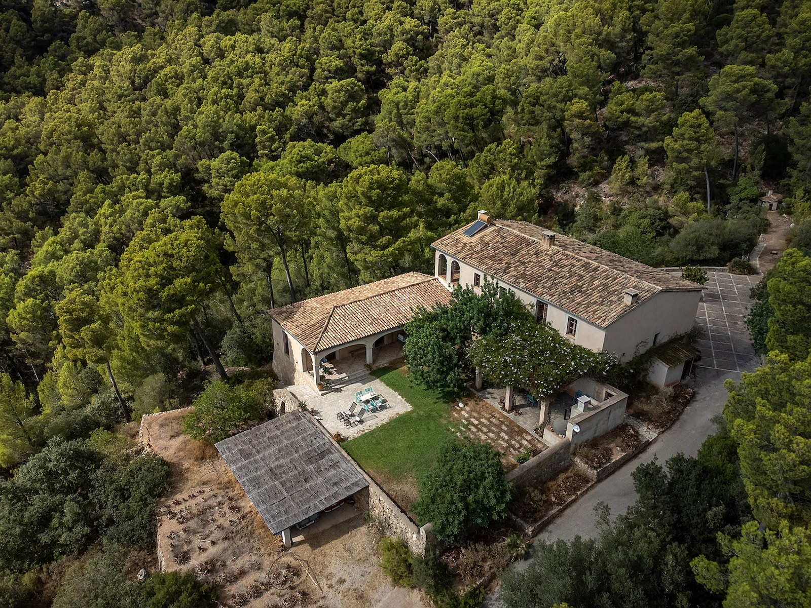 Vue de dessus d'une maison en pierre avec toit de tuiles, entourée d'une forêt de pins dense.