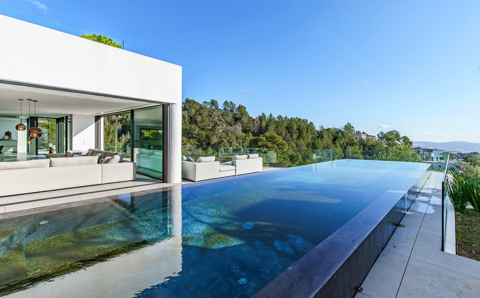 Villa de luxe avec piscine à débordement, terrasse vitrée et salon moderne surplombant une forêt.