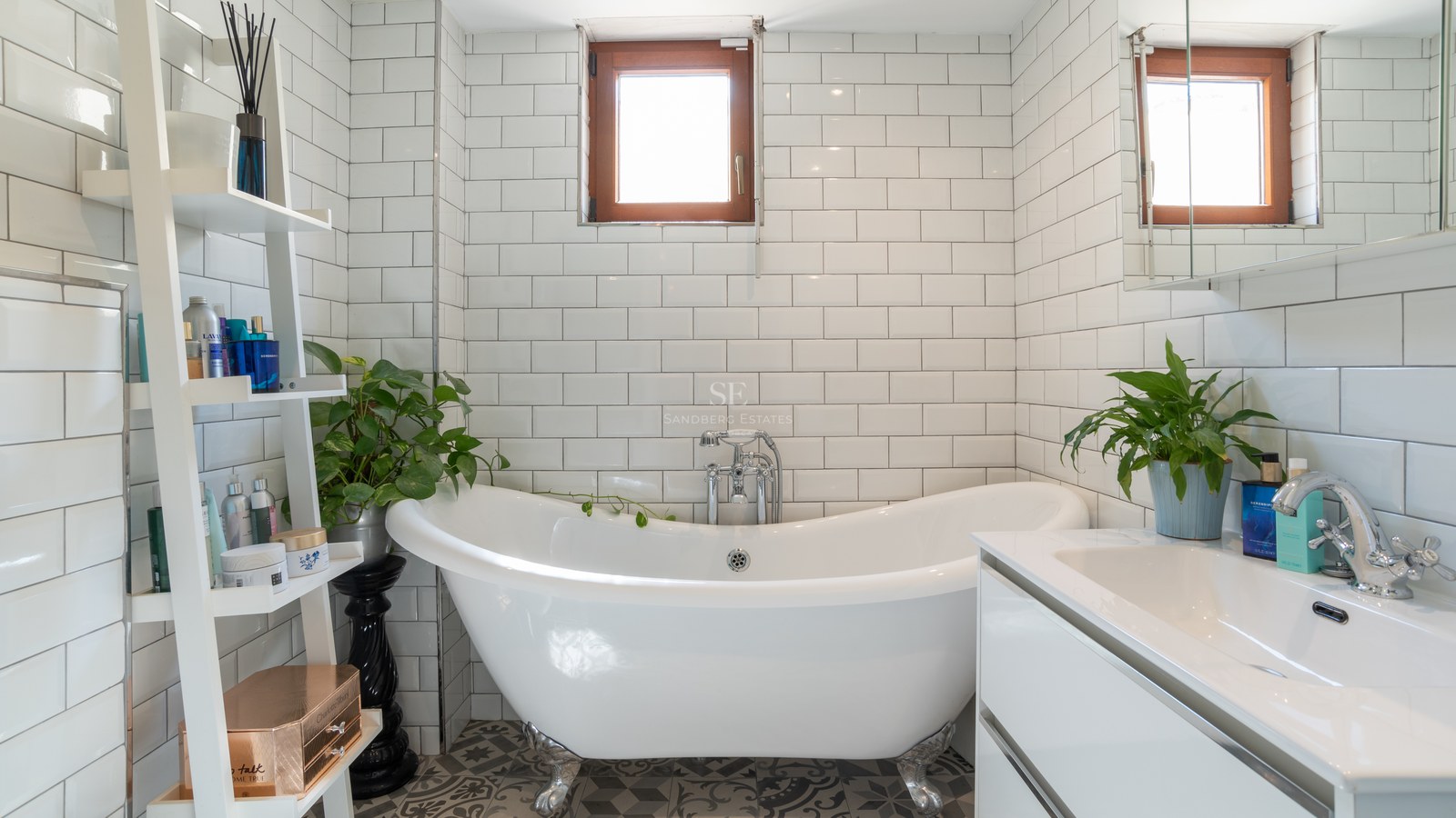 Baño luminoso con bañera exenta de patas, azulejos tipo metro y mueble de lavabo moderno blanco.