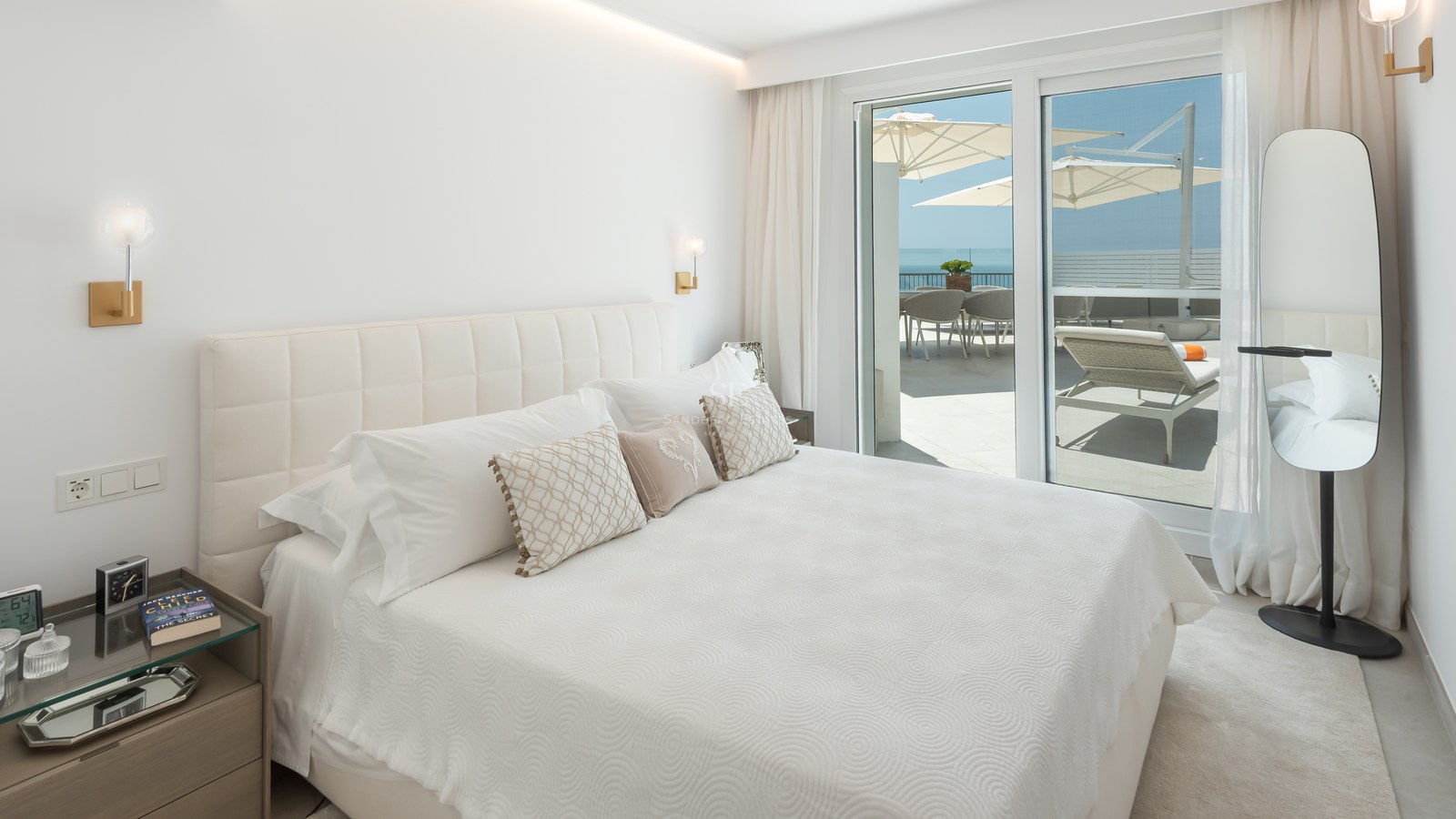 Bright master bedroom featuring a white tufted headboard and glass doors opening to a sun-drenched terrace with sea views.