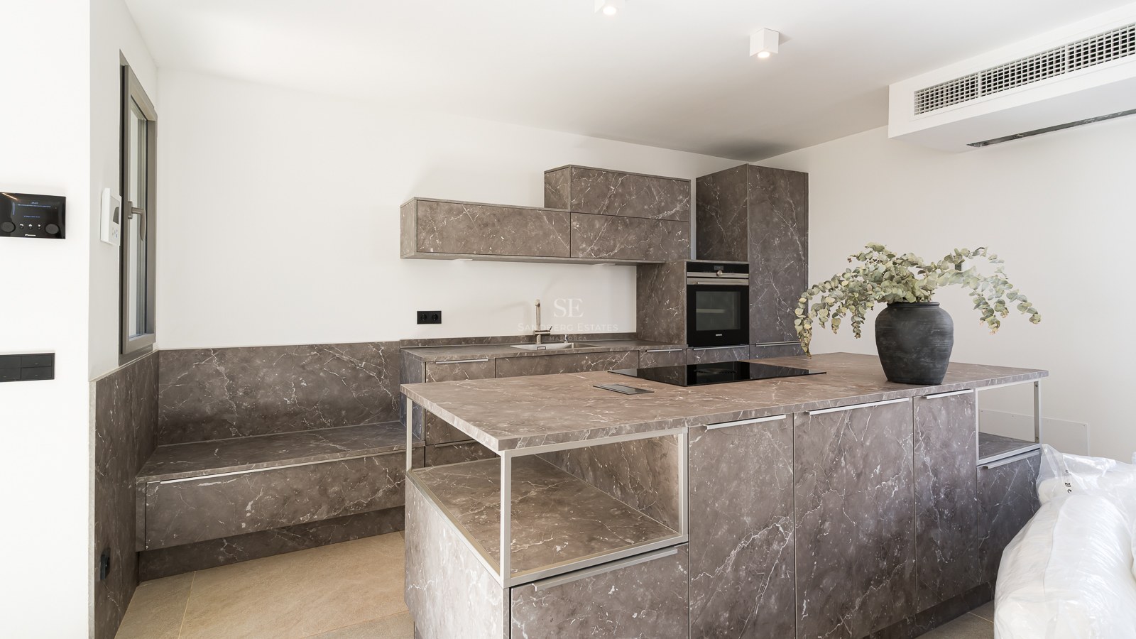 Moderne Küche mit großer Insel in grau gemasertem Stein, integrierten Geräten und minimalistischen weißen Wänden.