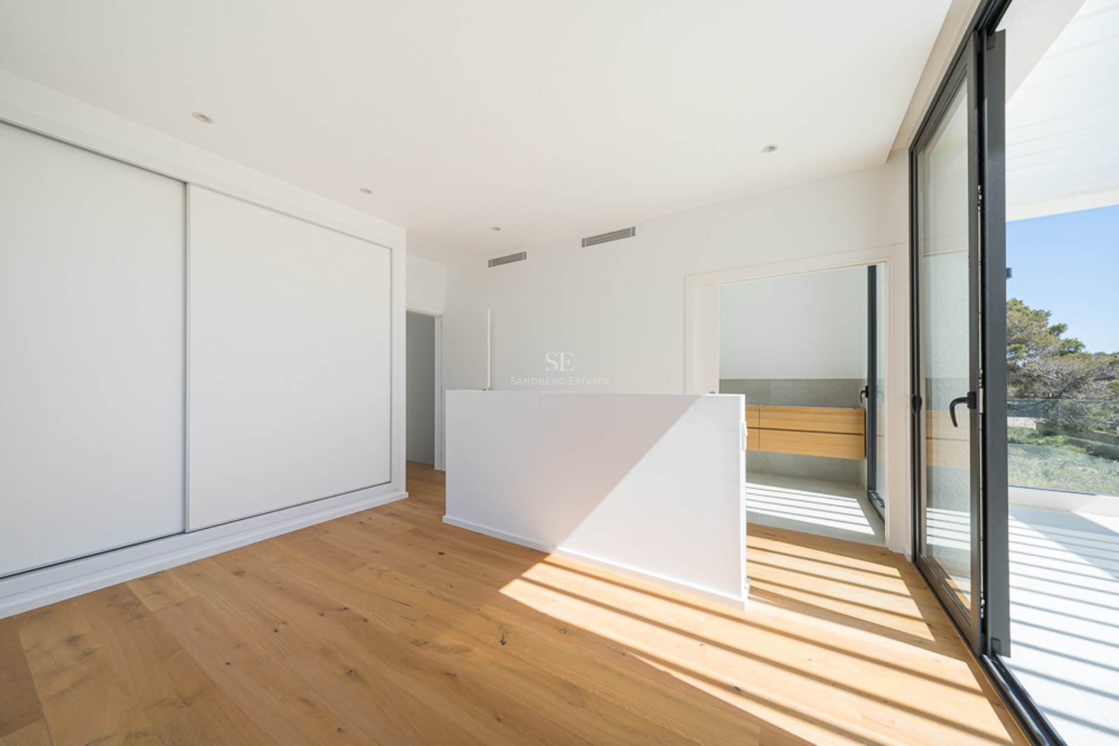 Chambre lumineuse avec parquet en chêne, placards blancs intégrés et grandes baies vitrées ouvrant sur une terrasse.
