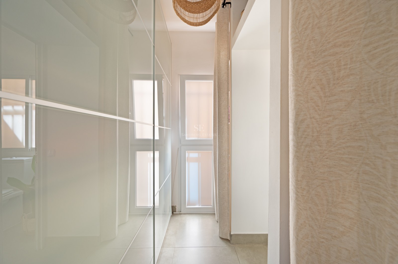 Hallway with floor-to-ceiling frosted glass wardrobes, beige floor tiles, and a wicker pendant light.