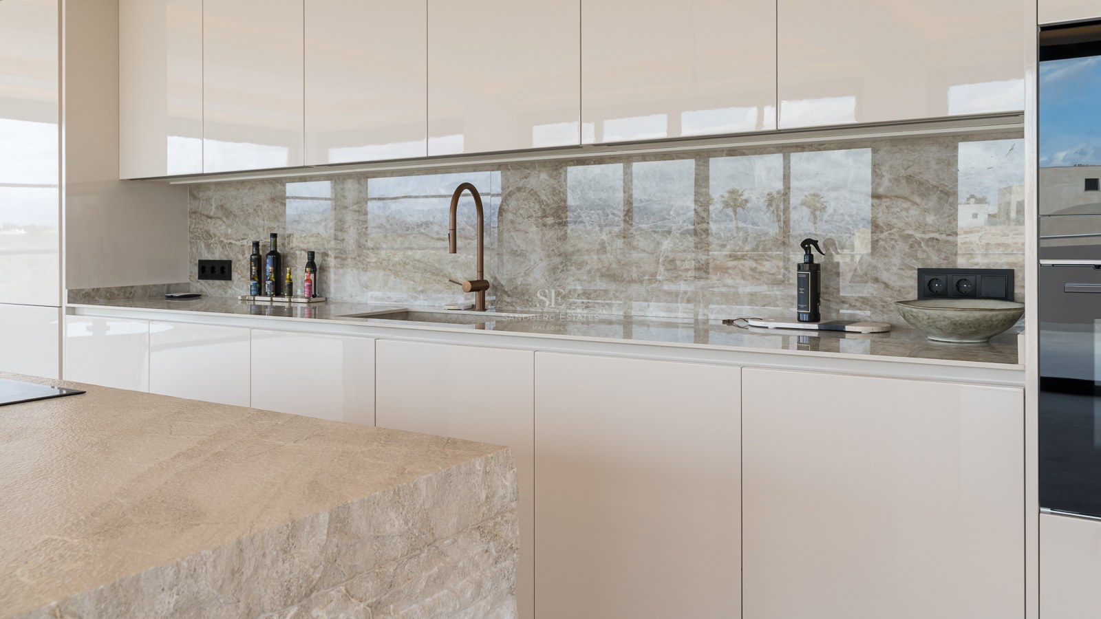 Contemporary kitchen featuring cream handleless cabinets, veined marble splashback, and a bronze designer tap.