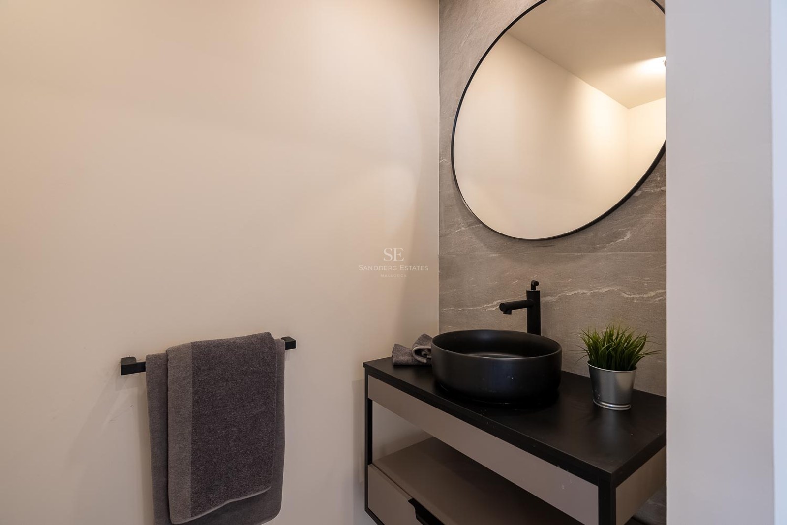 Salle de bains moderne avec miroir circulaire, vasque noire et carrelage mural effet pierre grise.