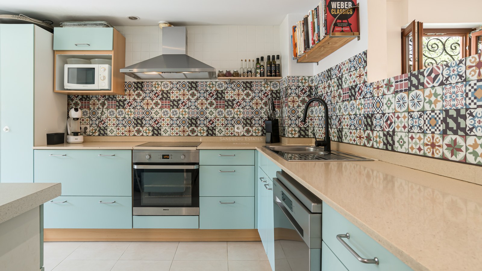 Cocina con muebles verde menta, encimera beige y azulejos decorativos de estilo hidráulico.